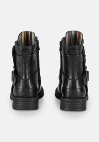 Botas de tobillo de cuero negro con un acabado mate, cremallera trasera, acentos de correas y forro de rayas multicolores visible en la parte superior.
