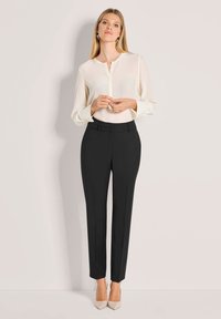 Cremefarbige Bluse mit V-Ausschnitt, schwarze maßgeschneiderte Hosen und beigefarbene spitze Absätze. Glattes Material, lange Ärmel und taillierte Passform.