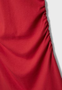 Tissu rouge vif froncé avec une texture lisse. Le design présente des sections rassemblées, créant une apparence fluide et contourée.