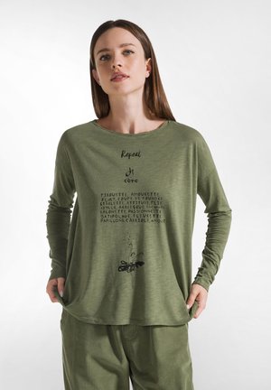 Haut vert à manches longues avec un col rond et un texte imprimé en noir, complété par un graphisme floral à l'ourlet. Porté avec un pantalon assorti.