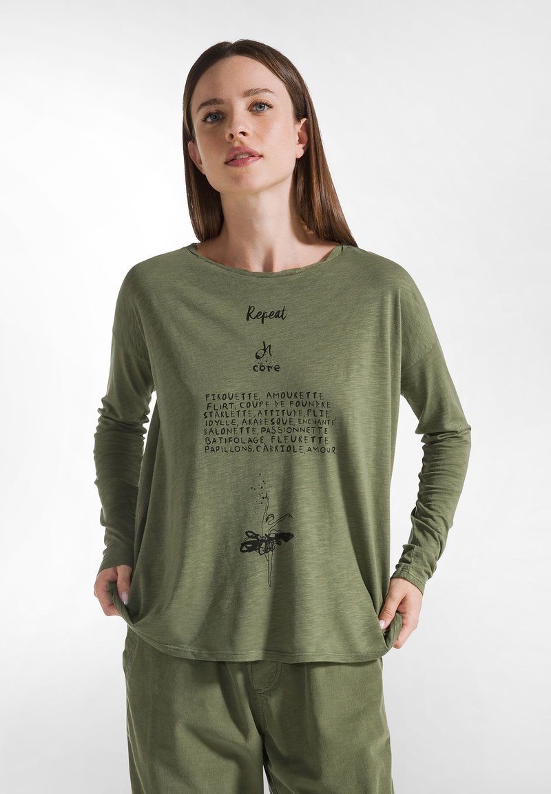 Grön långärmad topp med rund halsringning och tryckt text i svart, kompletterad med en blommig grafik i nederkant. Bärs tillsammans med matchande byxor.