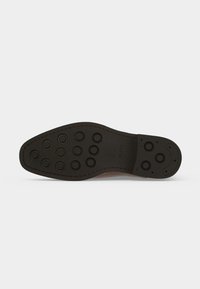 Semelle de chaussure noire avec des motifs circulaires antidérapants et des coutures le long du bord sur un fond clair uni.