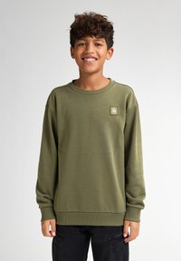 Olijfgroene sweatshirt met lange mouwen, ronde hals en ribgebreide manchetten. Voorzien van een vierkant logo patch op de linkerborst. Zachte stoftextuur.