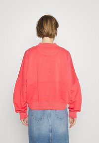 Sudadera corta de color coral con cuello redondo y hombros caídos, combinada con una falda de mezclilla azul. Textura suave y diseño casual.