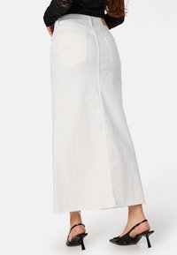 Gonna maxi in denim bianco con forma dritta, orlo sfilacciato e tasche posteriori. Abbinata a scarpe con tacco nere.