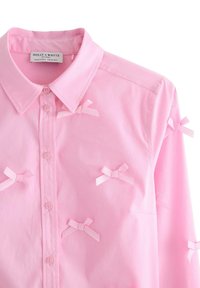 Camicia rosa con bottoni, realizzata in cotone, con colletto e nastri decorativi cuciti sulla parte anteriore. Tessuto morbido, vestibilità standard.