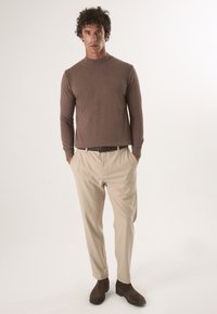 Bruine gebreide trui, beige broek, donkerbruine enkellaarsjes. Eenvoudig ontwerp met een aansluitende pasvorm en geribbelde details bij de kraag.