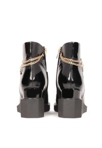 Bottines en cuir verni noir avec une finition brillante, talons carrés, accents en chaîne dorée et fermetures éclair à l'arrière.