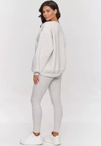 Jasnoszara, oversizowa bluza i pasujące legginsy, wykonane z miękkiego materiału. Posiada długie rękawy, żeberkowe mankiety i białe sneakersy.