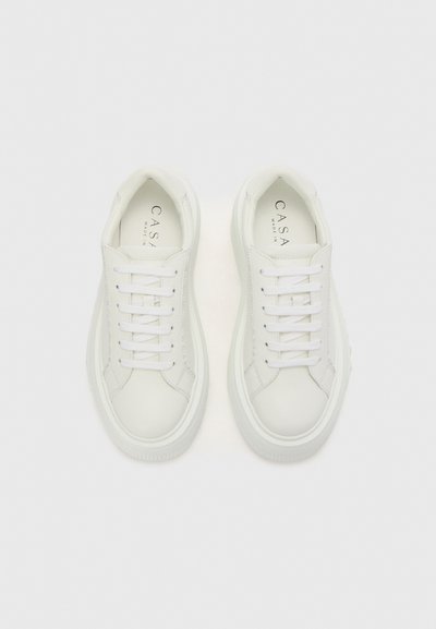 White leather sneakers with flat laces, rounded toe, textured rubber sole, and subtle brand logo inside. Clean design, minimalistic appearance.