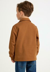 Brun långärmad skjorta med krage, gjord av mjukt tyg, i kombination med blå denimjeans, sedd bakifrån.