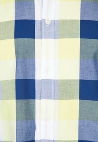 Camicia a maniche corte a quadri con strisce verdi, blu e gialle, dotata di una patta dei bottoni bianca e una trama del tessuto liscia.