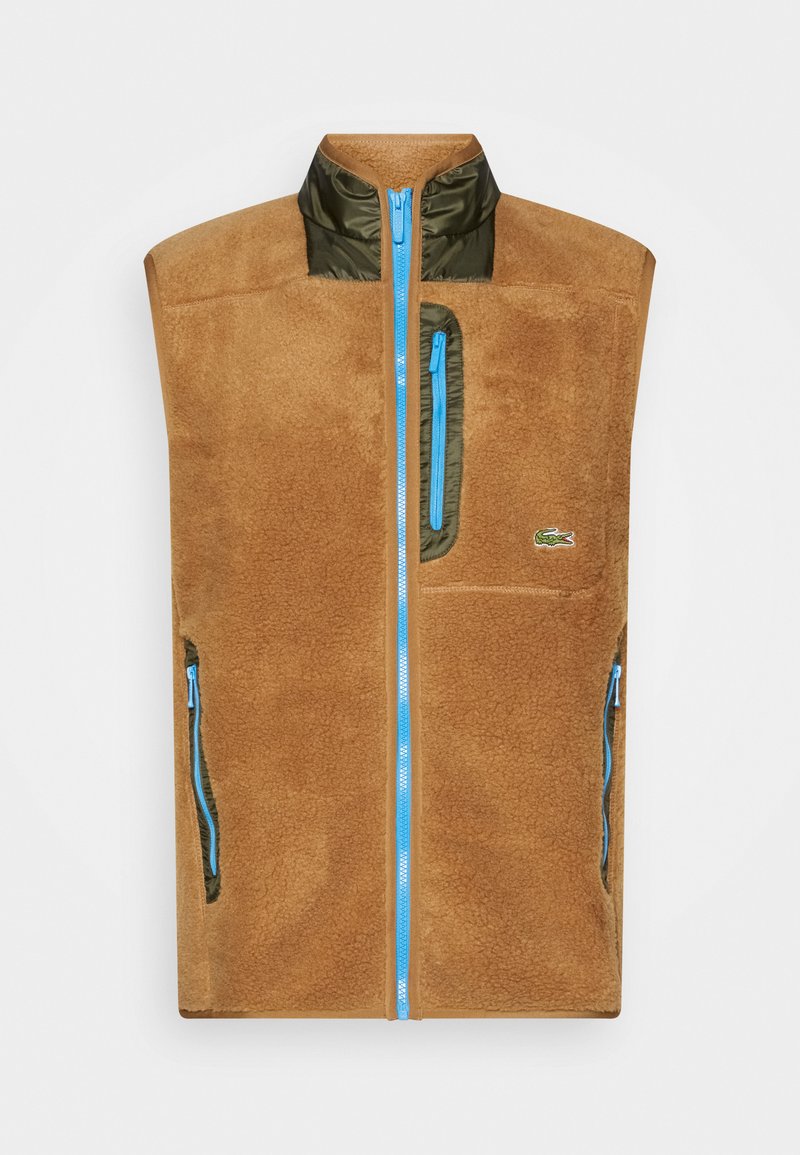 Gilet en polaire marron et olive, doté d'un col montant, d'une fermeture éclair bleue et de plusieurs poches zippées. Logo Lacoste sur la poitrine.