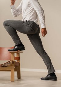 Grå skræddersyede bukser med en glat tekstur, parret med polerede sorte sko. En hvid langærmet skjorte fuldender outfittet.