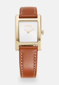 Montre rectangulaire dorée avec un cadran blanc, un bracelet en cuir marron et des coutures claires. Présente des aiguilles dorées minimalistes et une couronne.