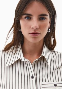 Hemd mit Knopfverschluss, das schmale braune Streifen auf einem cremefarbenen Hintergrund zeigt, mit einem klassischen Kragen und einer einzelnen Brusttasche.