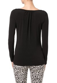 Maglietta nera a maniche lunghe con scollo a barchetta e dettaglio arricciato sul retro, abbinata a pantaloni a stampa leopardata bianca e nera.