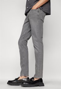 Smal passform grå jeans med en subtil tekstur, med frontlommer og et rent design. Kombinert med polerte sorte loafers.