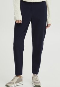 Navy blue pants with a tailored design, featuring a smooth texture and a tapered leg, paired with light-colored sneakers and a cream sweater.