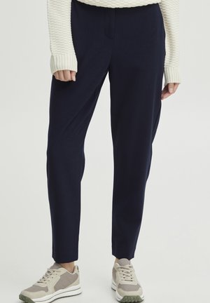 Navy blue pants with a tailored design, featuring a smooth texture and a tapered leg, paired with light-colored sneakers and a cream sweater.