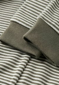 Green and white striped fabric with ribbed cuffs. Features a soft texture and horizontal lines, emphasizing a layered design.