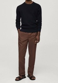 Tmavě modrý žebrovaný svetr, hnědé přizpůsobené kalhoty a černé sandály. Tento outfit má jednoduchý, ale moderní design s čistými liniemi.