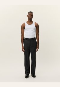 Zwarte broek met een getailleerde pasvorm, gecombineerd met een wit tanktop. De stof is soepel en de broek heeft een subtiele glans. Zwarte schoenen maken de look compleet.
