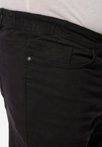 Pantalones de algodón negros con una cinturilla elástica, bolsillos laterales y traseros, y una textura suave, con un detalle de cierre a presión seguro.