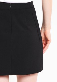 Svart mini kjol med en ren design, mjuk tyg och två sidofickor. Sömmen är något fransad och den har en dragkedja bak.