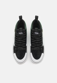 Sneaker alte nere e verdi con upper in suede, suola in gomma bianca, lacci con motivo e doppi gancetti sul tallone.