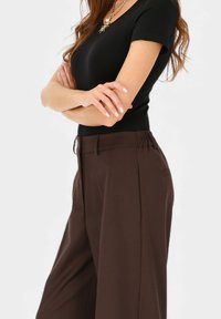 Brązowe spodnie o szerokich nogawkach i gładkiej fakturze, z wysokim stanem i bocznymi kieszeniami. Połączone z dopasowanym czarnym topem.