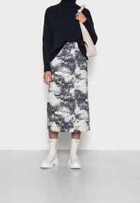 Navy coltrui, gemusterde midi-rok in wit en navy, witte enkellaarsjes met chunky zolen, en een lichte tas.