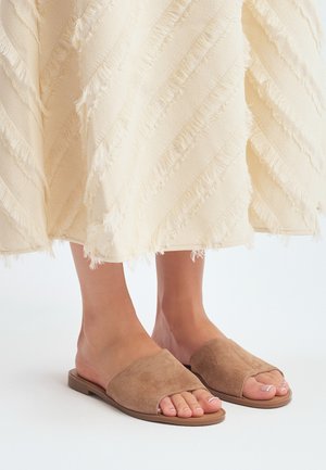 Tan suède slide sandalen met een open teenontwerp en een platte zool, gecombineerd met een textuur rok in crèmekleur met rafelige randen.