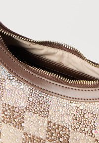 Καφέ τσάντα χειρός με χρυστό φερμούαρ, με υφασμάτινη επιφάνεια διακοσμημένη με πολλά μικρά λαμπερά στρας.