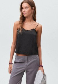 Črna satenska majica s čipkastim robom, z zmernimi naramnicami in sproščenim krojem, v kombinaciji s sivo hlačami in svetlo sivo jopico.