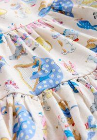 Lähivaade kangast, millel on värvilised loomade illustratsioonid, sealhulgas sinine täpilise mustriga elevant, kes mängib harfi, ja teised fantaasiarikkad olendid.