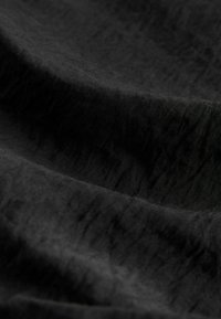 Fekete szövet, amelynek enyhén gyűrött textúrája van, puha, matt felületekkel és finom árnyalatváltozásokkal az anyagon.