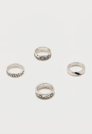 Cztery srebrne pierścionki z czarnymi grawerowanymi wzorami, w tym słońcem, falami, wzorem geometrycznym oraz detalem pióra, na białej powierzchni.