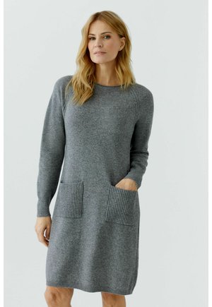 Grijze gebreide jurk met lange mouwen, geribbelde accenten op de mouwen en twee voorzakken. Zachte textuur, knielengte, relaxed fit.