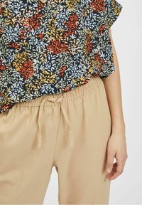 Kukkakuvioinen musta paita, jossa on monivärisiä lehtiä, yhdistettynä beigekulhoisiin elastisiin housuihin, joissa on nyöri. Pehmeä kangas ja rento leikkuu.