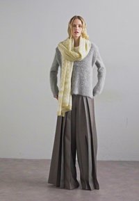 Pulover gri pufos, fular crem și pantaloni maro plisați. Puloverul are o textură; fularul are un model subtil; pantalonii sunt evazați.