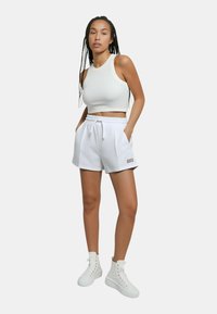 Crop top sportivo bianco con texture a coste, abbinato a pantaloni corti bianchi a vita alta con tasche laterali e cordino. Sneakers bianche.