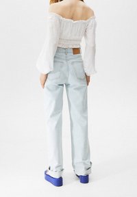 Hvid off-shoulder bluse med flæsekanter, parret med lyseblå højtaljede jeans og blå plateau sko. Synlige rygdetaljer.