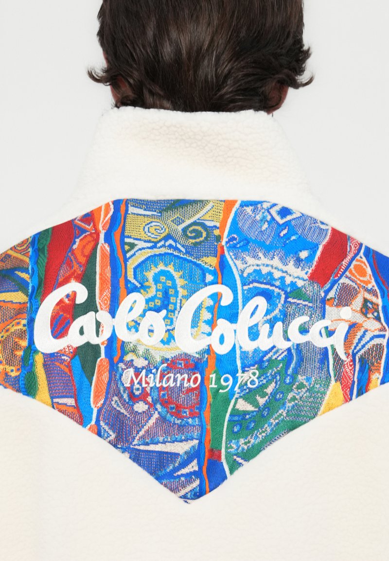 Chaqueta de forro polar blanca con un diseño colorido en la parte posterior que presenta patrones en azul, verde, rojo y naranja, con el texto "Carlo Colucci Milano 1978".