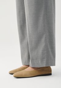 Tan semskede sko med rund tå og flat såle, kombinert med grå vide bukser med en jevn tekstur.