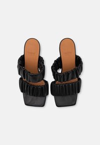 Czarne sandały na obcasie z dwoma falbanowymi paskami i kwadratowymi czubkami. Wierzch ma błyszczącą fakturę, podczas gdy wkładka jest gładka i w kolorze opalonemu.