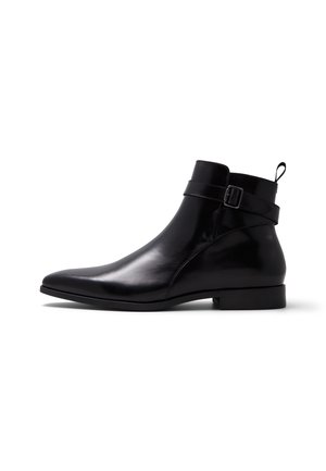 Schwarzer, polierter Leder-Stiefel mit spitzer Zehenpartie, seitlichem Schnallenriemen, kleinem Absatz und Zuglasche an der Ferse, im Profil vor weißem Hintergrund dargestellt.