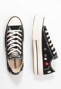 Czarne płócienne trampki z białymi sznurówkami i kauczukowymi podeszwami, z kolorowymi haftami kwiatowymi i kontrastującymi białymi detalami przeszyciami.