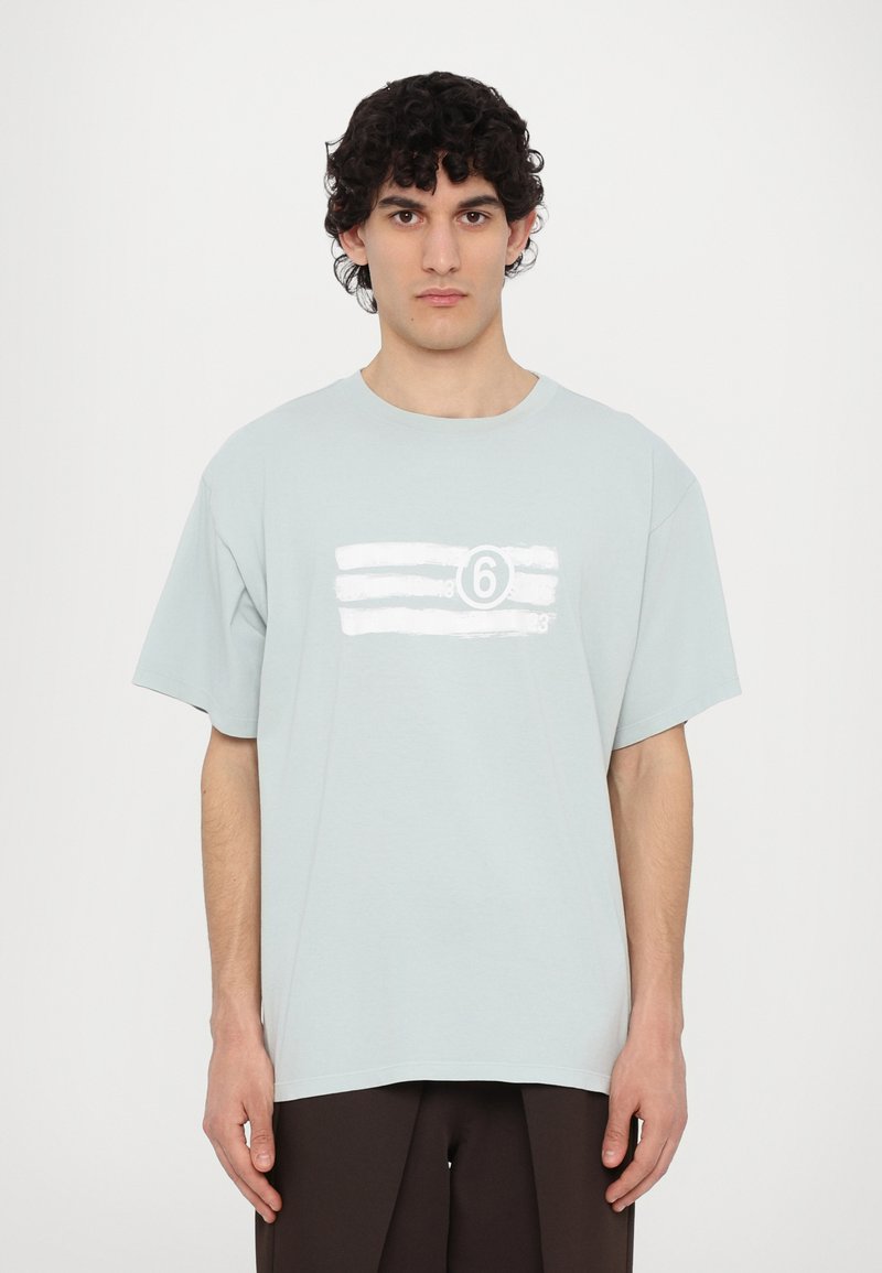 Ανοιχτό μπλε T-shirt με στρογγυλή λαιμόκοψη, χαλαρή εφαρμογή και λευκές γραφικές ρίγες καθώς και τον αριθμό "6" στη μπροστινή πλευρά. Κοντά μανίκια, μαλακή υφή.
