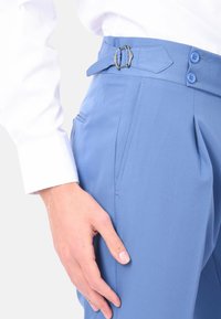 Pantaloni azzurri chiari con una cintura dotata di fibbia metallica, davanti piatto, due tasche laterali e una vestibilità sartoriale. Il tessuto ha una texture liscia.